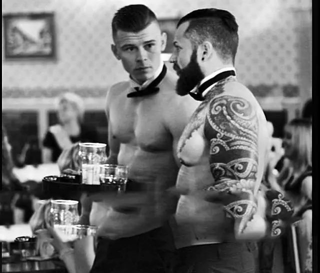 Two butlers in the buff serving drinks